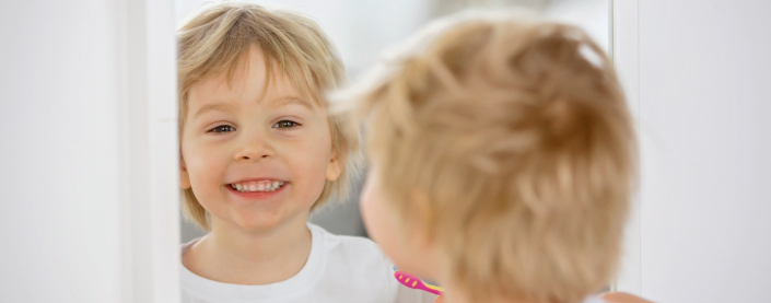 Child smiling in the mirror while holding his Spinbrush kids toothbrush.