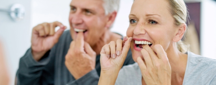 Couple flossing their teeth in the morning to help remove plaque on their teeth.