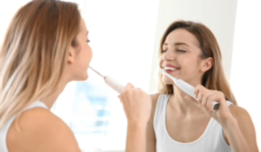 Smiling woman brushes her teeth with an electric toothbrush.